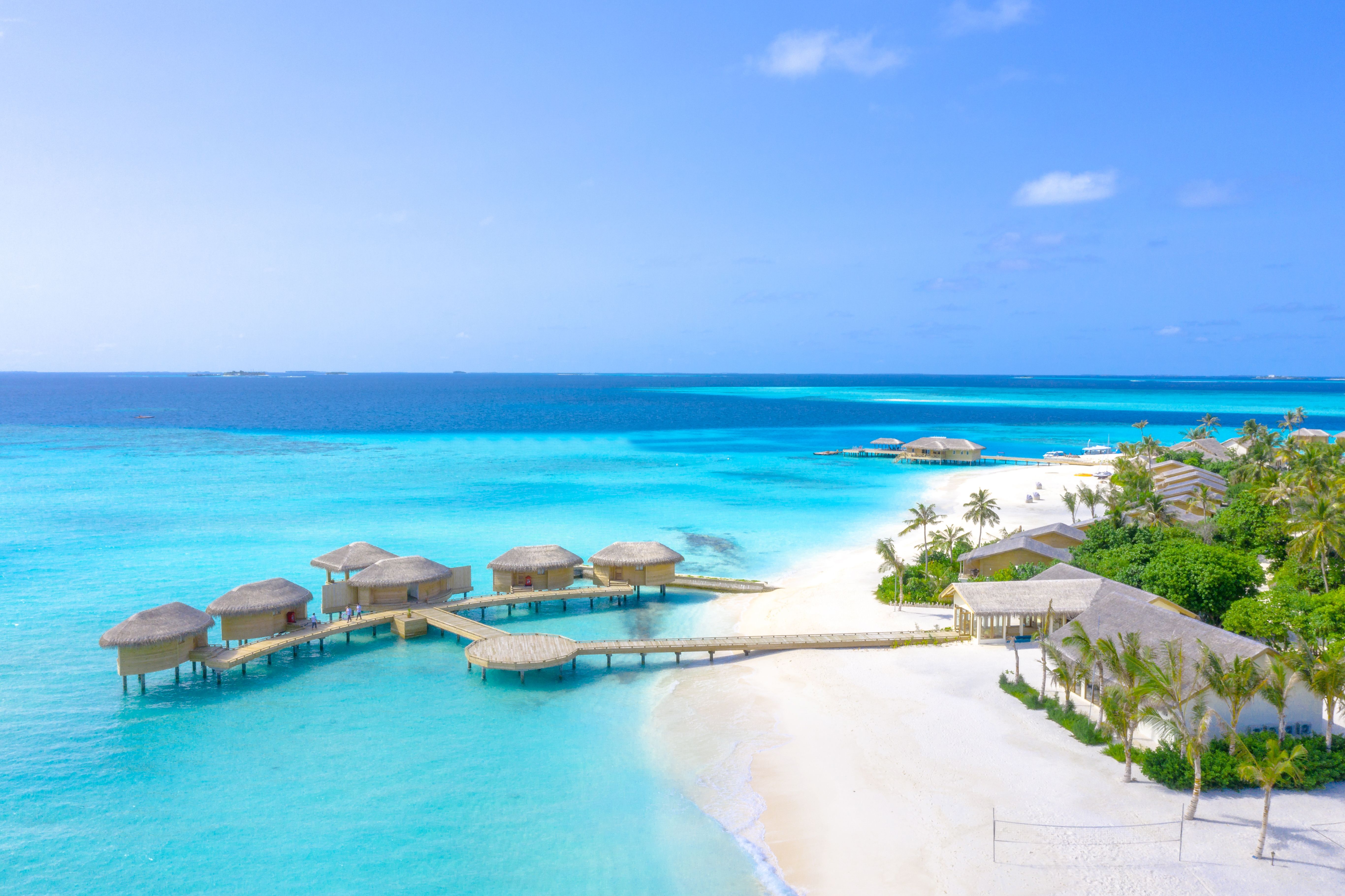 Aerial view of luxury overwater bungalows on turquoise ocean next to a white sand beach.