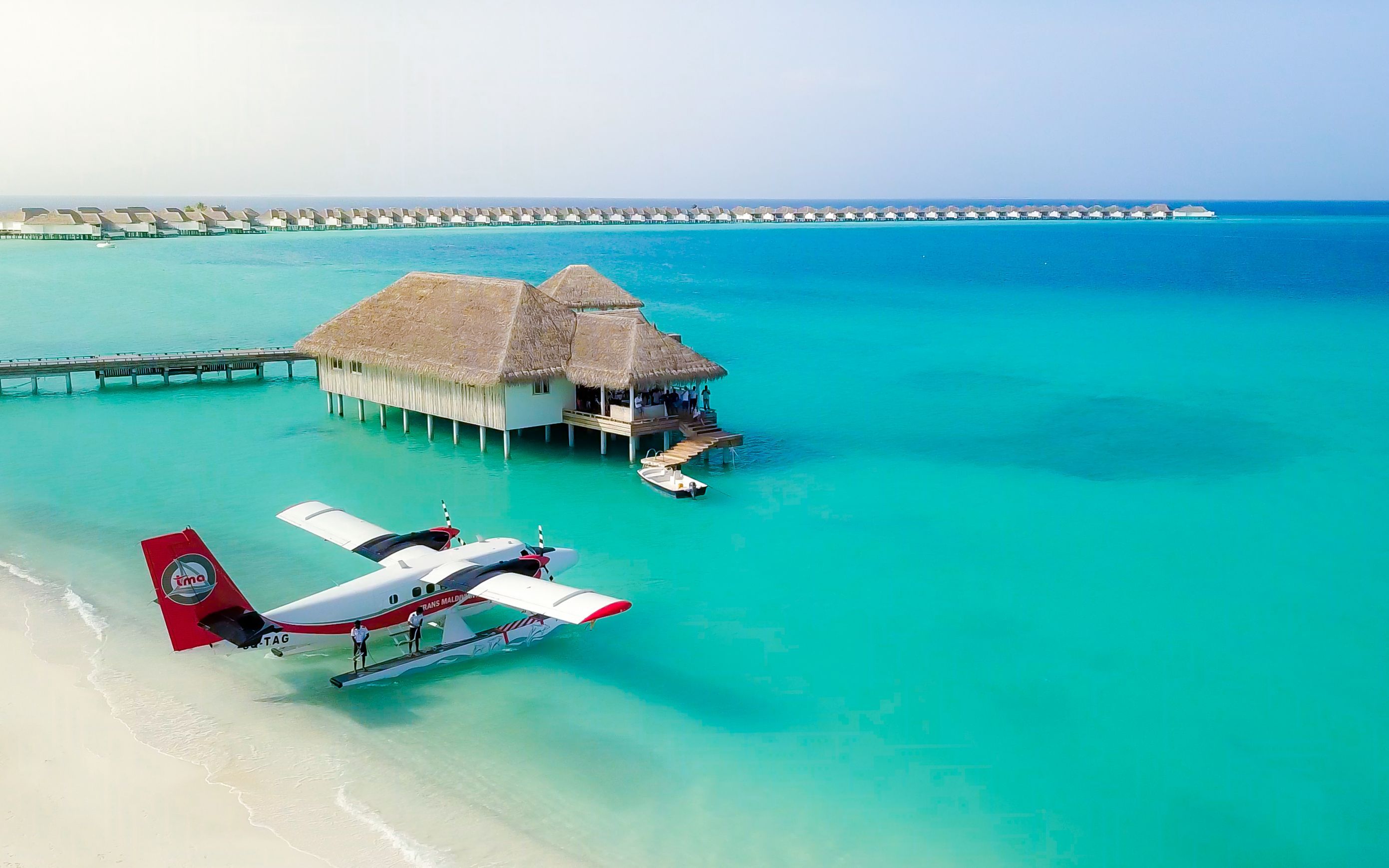 Seaplane on a white sandy beach next to overwater bungalows in turquoise ocean.